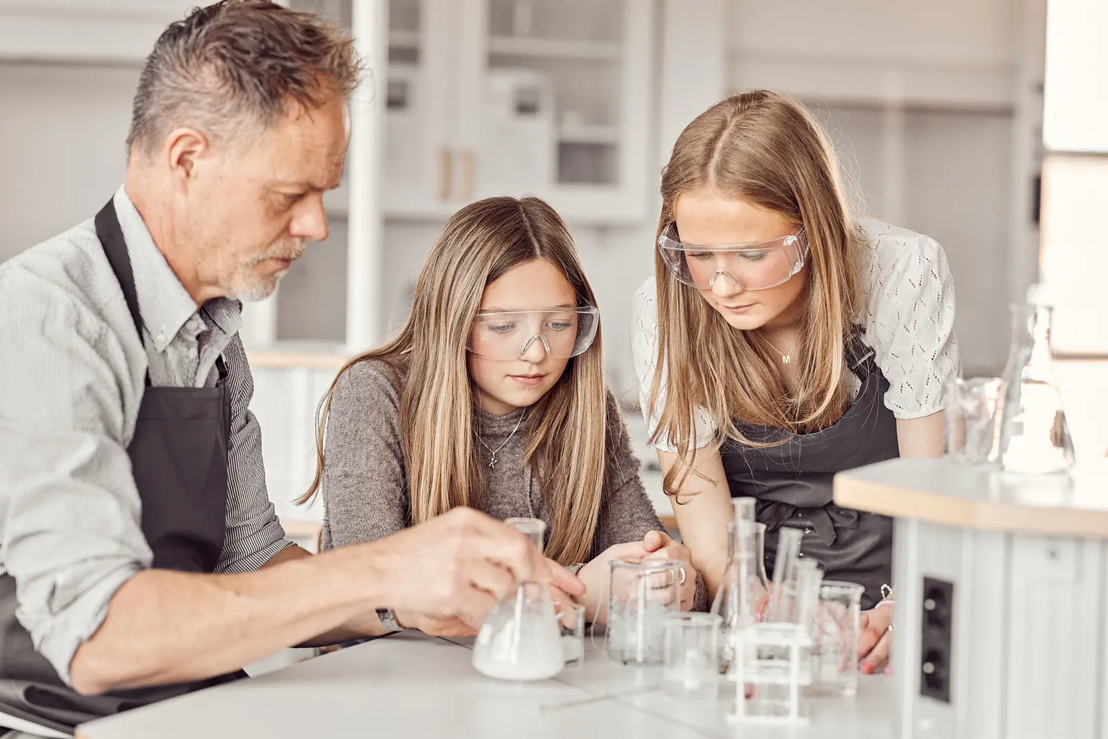 En lärare och två elever med skyddsglasögon gör ett kemiexperiment