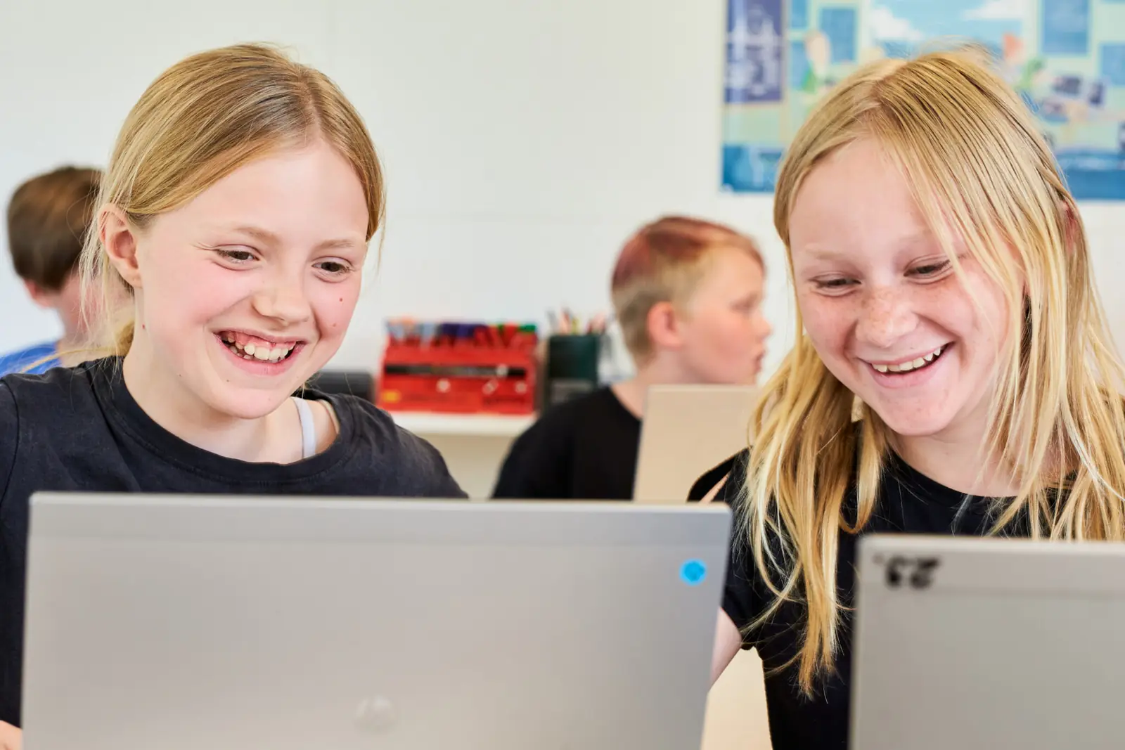Två elever skrattar tillsammans framför sina datorer i klassrummet